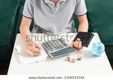 Kid teen boy counting money and taking notes, saving money in a piggy bank. Learning financial responsibility and projecting savings. Concept of finance, business, investment. Lessons in mindfulness