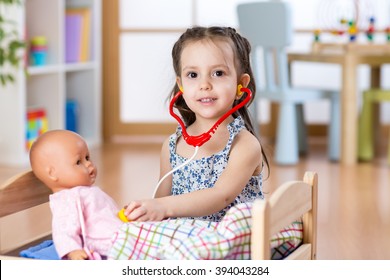 Kid toddler playing doctor role game examining her doll using stethoscope sitting in playroom at home, school or kindergarten