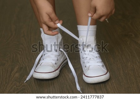 Kid tying shoes. Little girl struggling to tie shoe laces. Child learning fine motor skills.