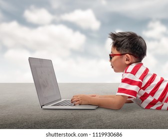 Kid Using A Laptop Computer With Sky Background.Asian Boy Wearing A Red T-shirt And Red Pants Wearing Glasses Is Using A Computer.concept Idea