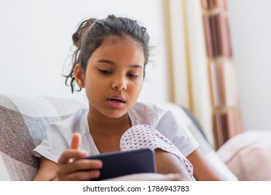 Kid Using Mobile Phone At Home, Lying On Sofa Relaxing On Weekend. Kid And Gadget Concept