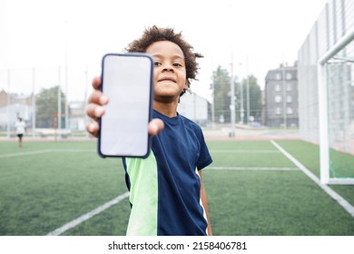 Kid Using Phone. Smiling And Excited Boy Showing Smartphone Empty Screen. Looking To Camera. Cellphone Display Mockup Mobile App Advertisement. African American Kid In Football Field. Blank Screen