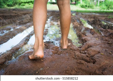 Kid Walking In Barefoot Through Muddy Road In Field