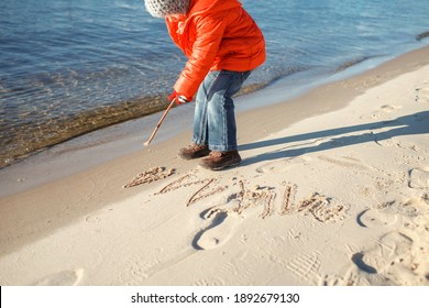 Kid Walking At The Beach In Winter, Drawing On Sand And Eating Croissant, Cold Temperature And Sunny Day, Love Keep You Warm, Happy Real People. Outdoors Lifestyle