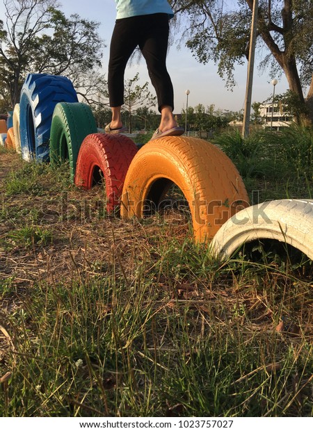 the kid walking on\
colourful balance car tires in playground. blue green red orange\
and white car tires. 