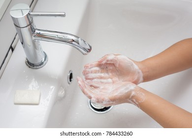 Kid Washing Hands In A White Basin With A Bar Of White Soap