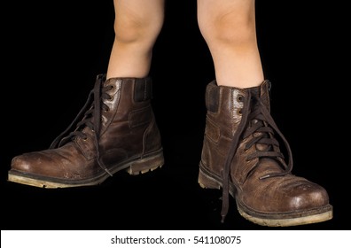 Kid Wearing A Pair Of Too Big Untied And Unpolished Brown Leather Boots, On Black