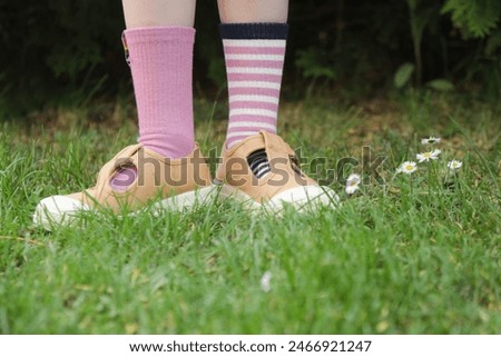 Kid wears different pair of socks. Child foots in mismatched socks standing outdoor.  Down syndrome awareness concept, odd socks day, anti-bullying week.