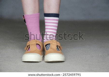Kid wears different pair of socks. Child foots in mismatched socks, studio photography. Down syndrome awareness concept, odd socks day, anti-bullying week.	