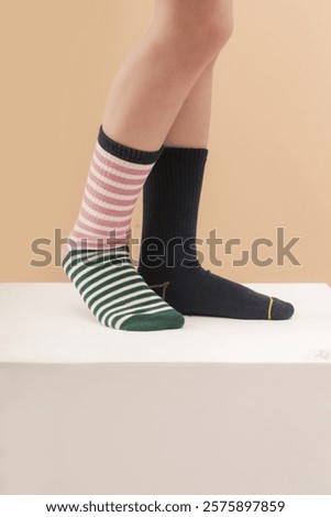 Kid wears different pair of socks. Child foots in mismatched socks, studio photography. Down syndrome awareness concept, odd socks day, anti-bullying week.	