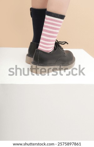 Kid wears different pair of socks. Child foots in mismatched socks, studio photography. Down syndrome awareness concept, odd socks day, anti-bullying week.	