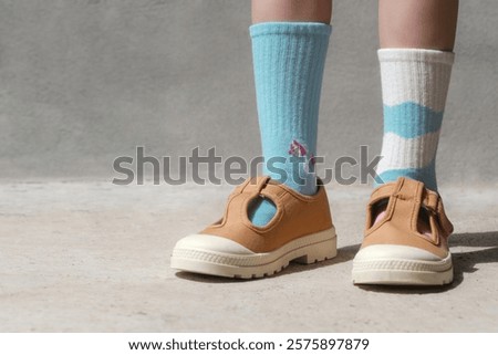 Kid wears different pair of socks. Child foots in mismatched socks, studio photography. Down syndrome awareness concept, odd socks day, anti-bullying week.	