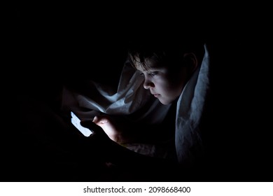 kid who plays games on the internet at night. Portrait of a teenager boy using mobile phone on dark bed. High quality photo. Bad habits of teenagers. Boy addicted with phone. - Shutterstock ID 2098668400