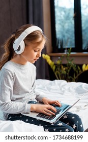 Kid In Wireless Headphones Using Laptop With E-learning In Bedroom