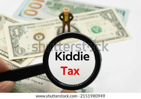 Kiddie Tax.Magnifying glass showing the words.Background of banknotes and coins.basic concepts of finance.Business theme.Financial terms.