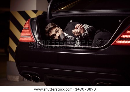 Kidnapped businessman. Tied up businessman lying in the car trunk and looking at camera