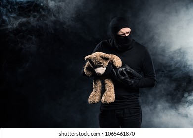 Kidnapper in balaclava holding gun and teddy bear