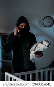 Kidnapper With Gun Holding Infant Child And Talking On Smartphone