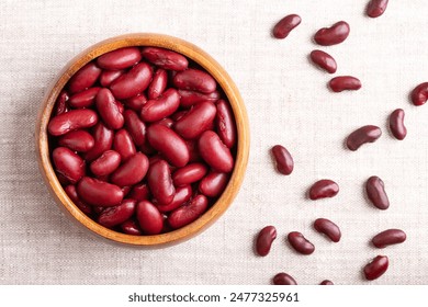 Kidney beans in a wooden bowl on linen fabric. Cooked and canned common kidney beans, a variety of the common bean Phaseolus vulgaris and vegetarian staple food. Dried uncooked beans on the right.