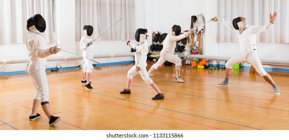 Kids with adults practicing effective fencing techniques in sparring in training room - Powered by Shutterstock