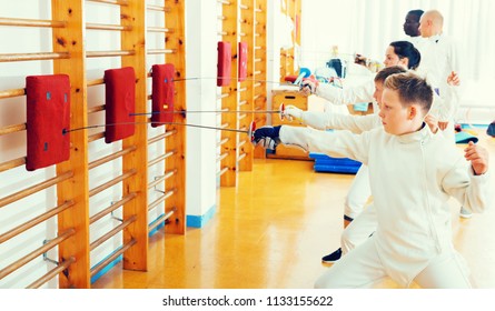 Kids with adults practicing effective techniques of fencing in training room
