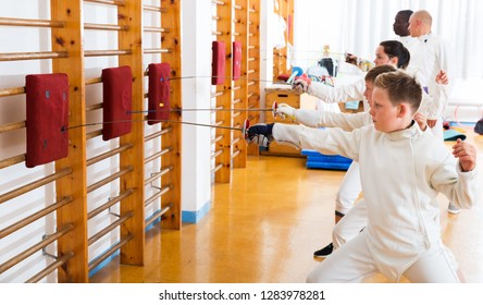 Kids with adults practicing effective techniques of fencing in training room