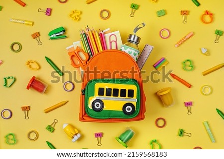 Kids Backpack with school bus on yellow background. Opened School backpack with stationery. Primary School or kindergarten. 