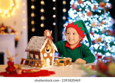 Kids baking Christmas gingerbread house. Children celebrating winter holiday at home. Decorated living room with fireplace and tree. Family activity. Little boy making cookies. - Powered by Shutterstock