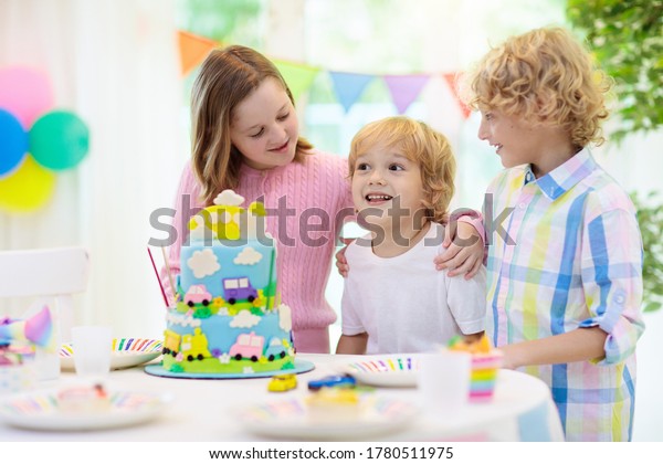 Kids birthday party. Boy cake with car and\
airplane. Child blowing out candles on colorful cake. Party\
decorations, rainbow flag banners, balloons. Vehicle theme\
celebration. Kid celebrating\
birthday