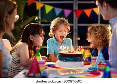 Kinder Geburtstagsfeier. Kind, das Kerzen auf Kuchen bläst und sich öffnet. Fest zum Thema "Pastel Regenbogen". Familie feiert zu Hause. Junge öffnete Geschenke, aß Kuchen. Süßigkeiten für Kinder.