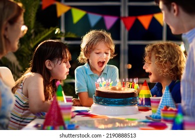 Kids birthday party. Child blowing candles on cake and opening presents. Pastel rainbow theme celebration. Family celebrating at home. Boy opening gifts, eating cakes. Sweets for children. - Powered by Shutterstock