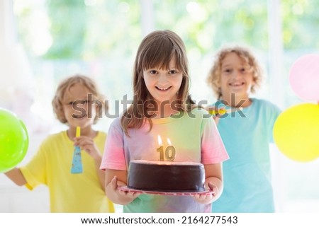Kids birthday party. Child blowing out candles on colorful cake. Little girl turning ten years old. Decorated home with rainbow flag banners, balloons. Family celebrating birthday. Party food.