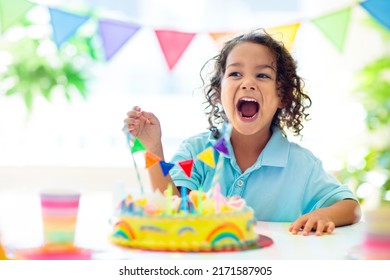 Kids birthday party. Children celebrate with colorful cake and gifts. Little curly boy blowing candles and opening birthday presents. Friends play with rainbow confetti. Party home decoration.