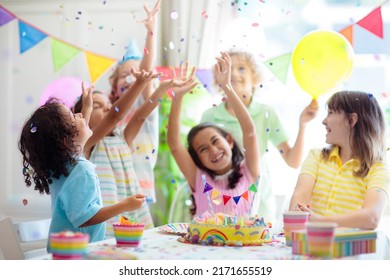 Kids Birthday Party. Children Celebrate With Colorful Cake And Gifts. Little Curly Boy Blowing Candles And Opening Birthday Presents. Friends Play With Rainbow Confetti. Party Home Decoration.