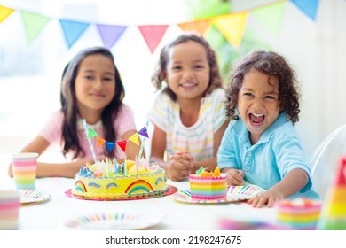 Kids Birthday Party. Children Celebrate With Colorful Cake And Gifts. Little Curly Boy Blowing Candles And Opening Birthday Presents. Friends Play With Rainbow Confetti. Party Home Decoration.