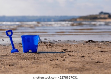 A kids blue bucket and spade by the shore on a Cornwall beach - Powered by Shutterstock