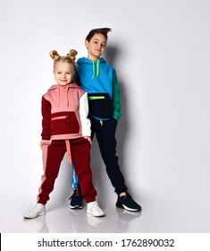 Kids, Boy And Girl, In Colorful Tracksuits And Sneakers. They Smiling, Posing Isolated On White Studio Background. Hands In Pockets. Childhood, Fashion, Advertising And Sport. Full Length, Copy Space