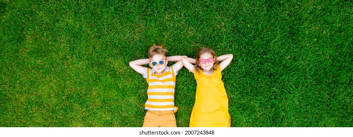 Kids boy and girl lying on the green grass. Happy children in cool yellow clothes from above. Top view. Child in sunglasses. Blond kids with freckles looking in camera - Powered by Shutterstock