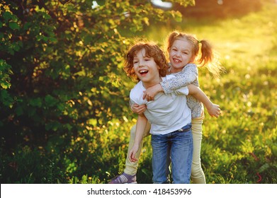 Kids, Boy And Girl Playing, Joking, Hogging And Having Fun At Sunset In The Park On The Green Grass. Children's Games, Leisure. 