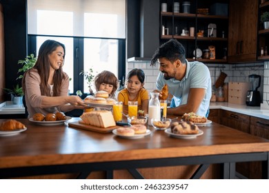 Kids at breakfast with parents. Mother is serving donuts on a plate. Cheerful family moments at home. - Powered by Shutterstock