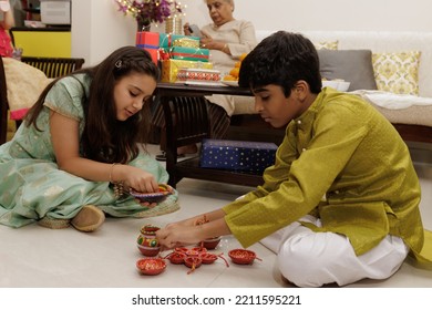 Kids, Brother Sister Friends Siblings Dressed Up In Ethnic Wear Arranging Diya Candle With Gift Box Celebrating Diwali Hindu Festival Laxmi Poojan With Ambient Light Bokeh