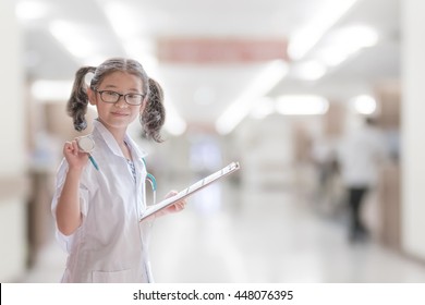 Kid's Career And Health Care, Medical Insurance Concept With Girl Child In White Doctor Or Nurse Lab Gown With Blurry Background Medical Clinic Healthcare Service Center Or Hospital