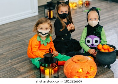 Kids in carnival costumes are celebrating Halloween, wearing face masks and playing with pumpkins and candies indoors