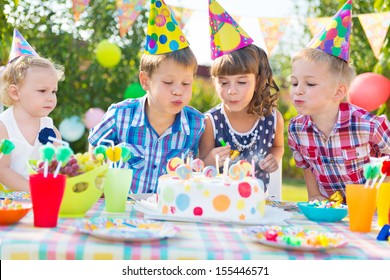 Kids Celebrating Birthday Party And Blowing Candles On Cake