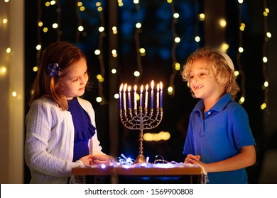 Kids Celebrating Hanukkah. Jewish Festival Of Lights. Children Lighting Candles On Traditional Menorah. Boy In Kippah With Dreidel And Sufganiyah Doughnut. Israel Holiday.