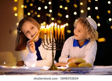 Kids celebrating Hanukkah. Jewish festival of lights. Children lighting candles on traditional menorah. Boy in kippah with dreidel and Sufganiyah doughnut. Israel holiday.