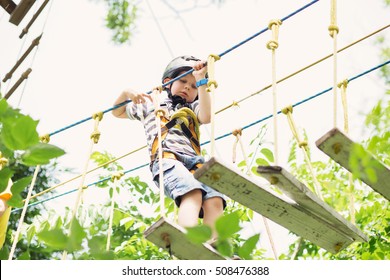 Kids Climbing In Adventure Park. Boy Enjoys Climbing In The Ropes Course Adventure. Child Climbing High Wire Park. Happy Boys Playing At Adventure Park, Holding Ropes And Climbing Wooden Stairs.