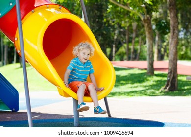 Kids climbing and sliding on outdoor playground. Children play in sunny summer park. Activity and amusement center in kindergarten or school yard. Child on colorful slide. Toddler kid outdoors.
