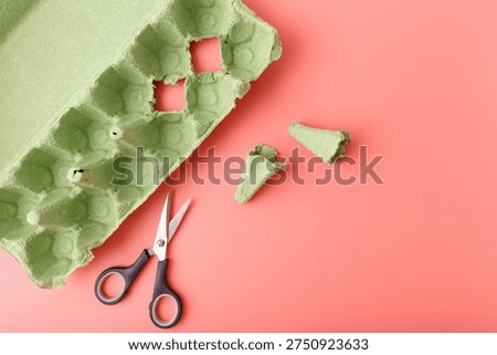 Kids craft process using green egg carton and scissors on pink background. Creative upcycling, recycled materials diy, school art project, sustainable education, zero waste hobby, handmade toy tutorial.