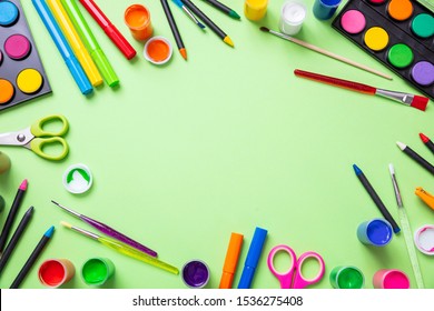 Kids creativity. Colorful paints and paintbrushes flat lay on pastel green color background, top view, copy space